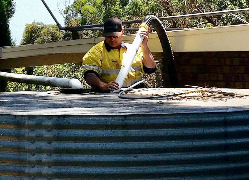 Wet vacuuming of water and waste from a rainwater tank being demonstrated by a member of the South Vac crew.